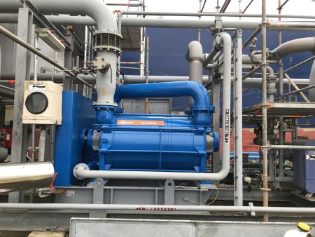 A blue liquid ring vacuum pump package installed on a skid amid process pipework and scaffolding.