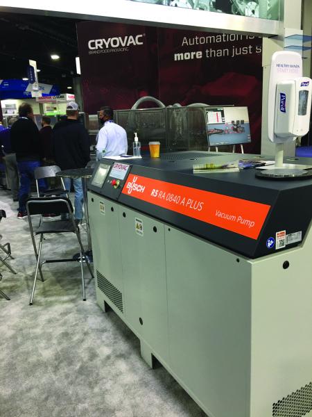 Trade show booth floor with a Busch R5 RA 0840 A Plus vacuum pump on display in front of a Cryovac branded backdrop, with attendees in the background.