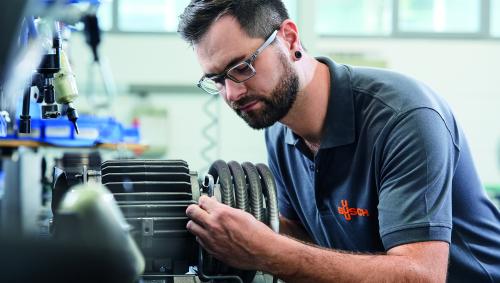A technician in a company polo shirt working on a compressor component at a workbench.