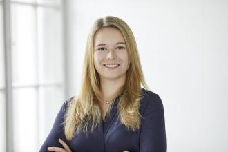 Lisa Glatt smiling in a navy blue top with arms crossed, in front of a bright window.