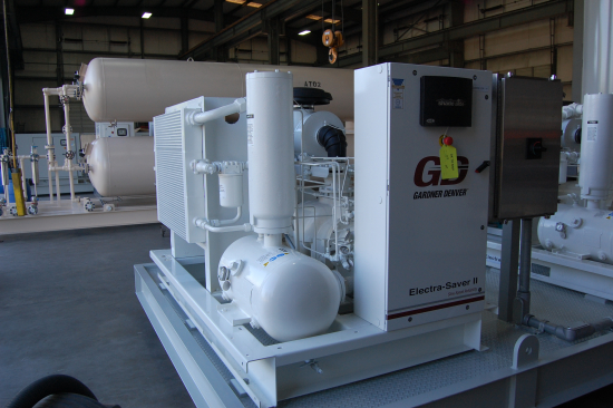 A Gardner Denver Electra-Saver II rotary screw compressor on a skid in a workshop, with receivers behind.