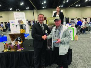 Two men shaking hands beside a raffle prize table at a trade show stand.