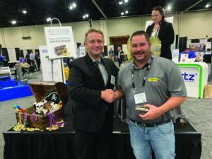 Two men shaking hands beside a raffle prize table at a trade show stand.